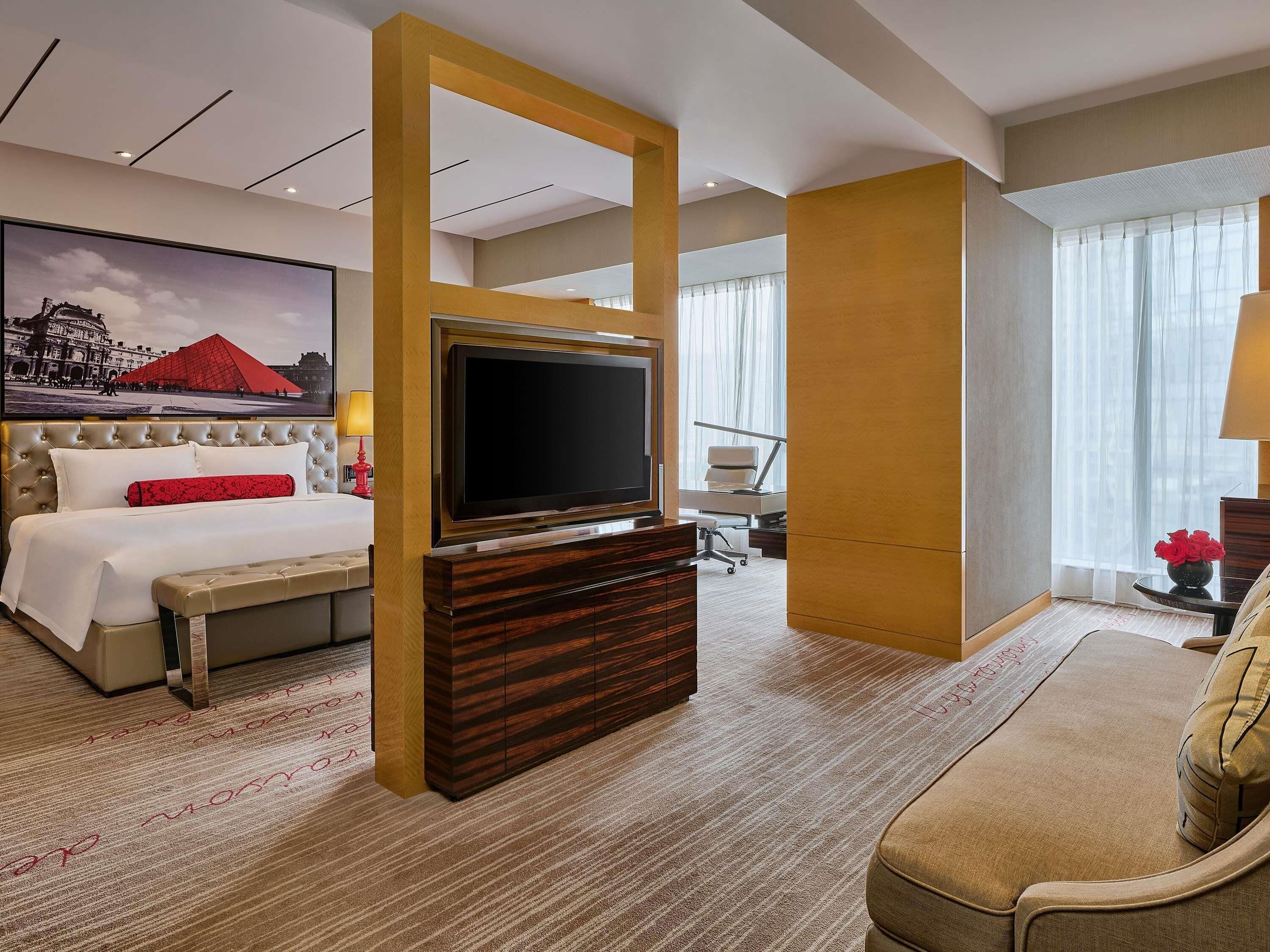 A hotel room with a bed, a TV, a desk, a chair, and a sofa.