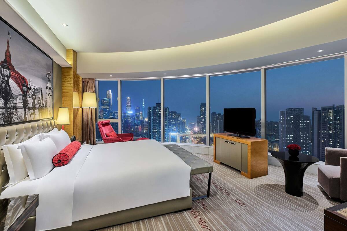 A modern hotel room with a large bed, a red chair, a desk, and a TV.