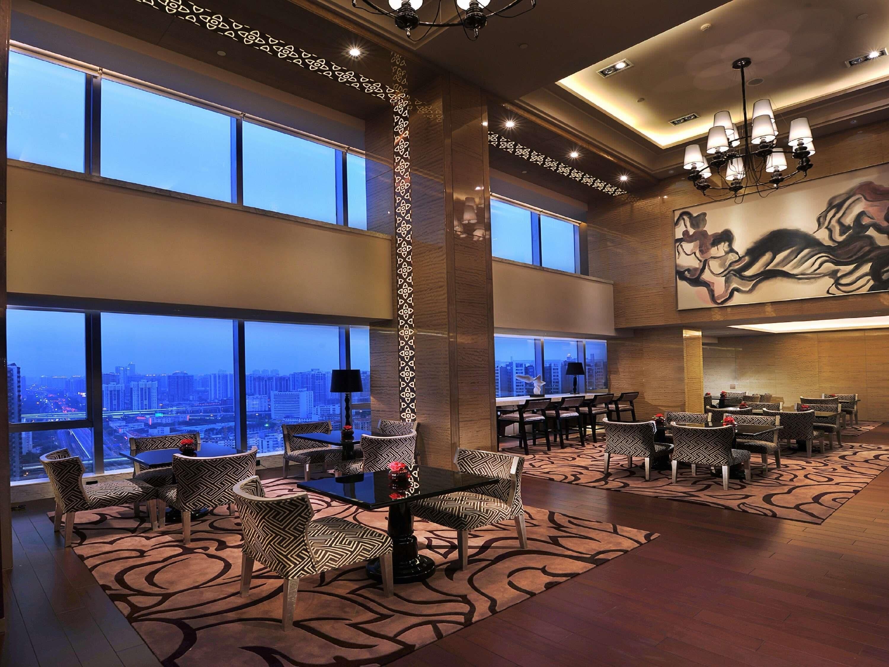 A spacious lobby with high ceilings, large windows offering city views, and a modern chandelier.