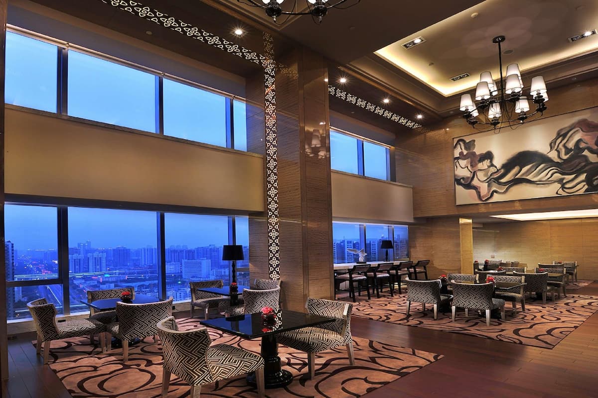 A spacious lobby with high ceilings, large windows offering city views, and a modern chandelier.