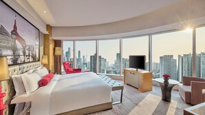 Habitación de hotel moderna con una cama grande, televisión, escritorio y vistas al horizonte de la ciudad.