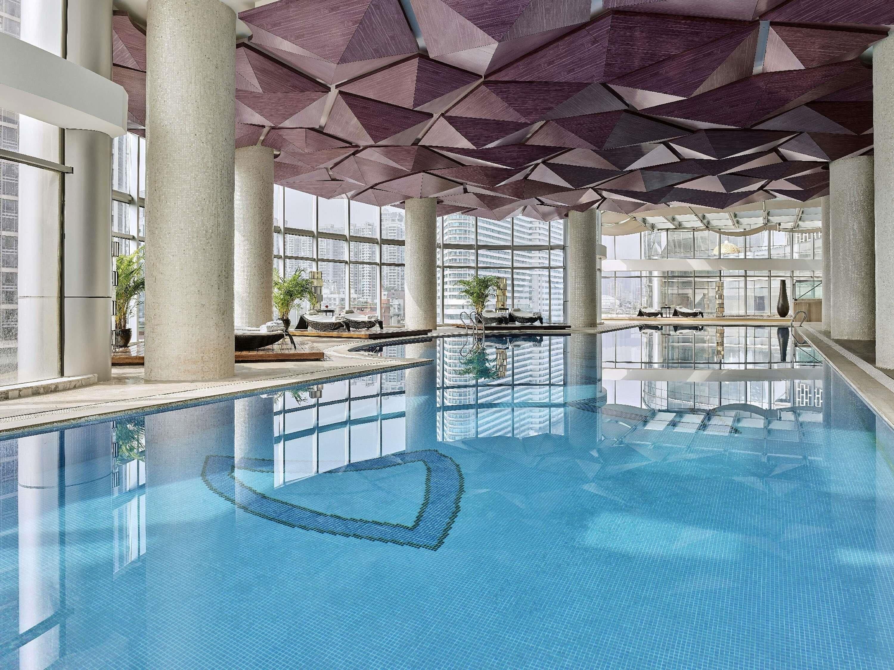 Une piscine intérieure dotée d’un plafond au design géométrique, de grandes fenêtres et d’équipements modernes.