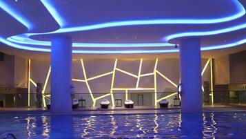 A modern hotel lobby with a pool, featuring a geometric light design on the walls and a glass railing around the pool.