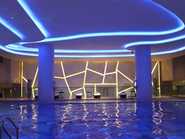 A modern hotel lobby with a pool, featuring a geometric light design on the walls and a glass railing around the pool.