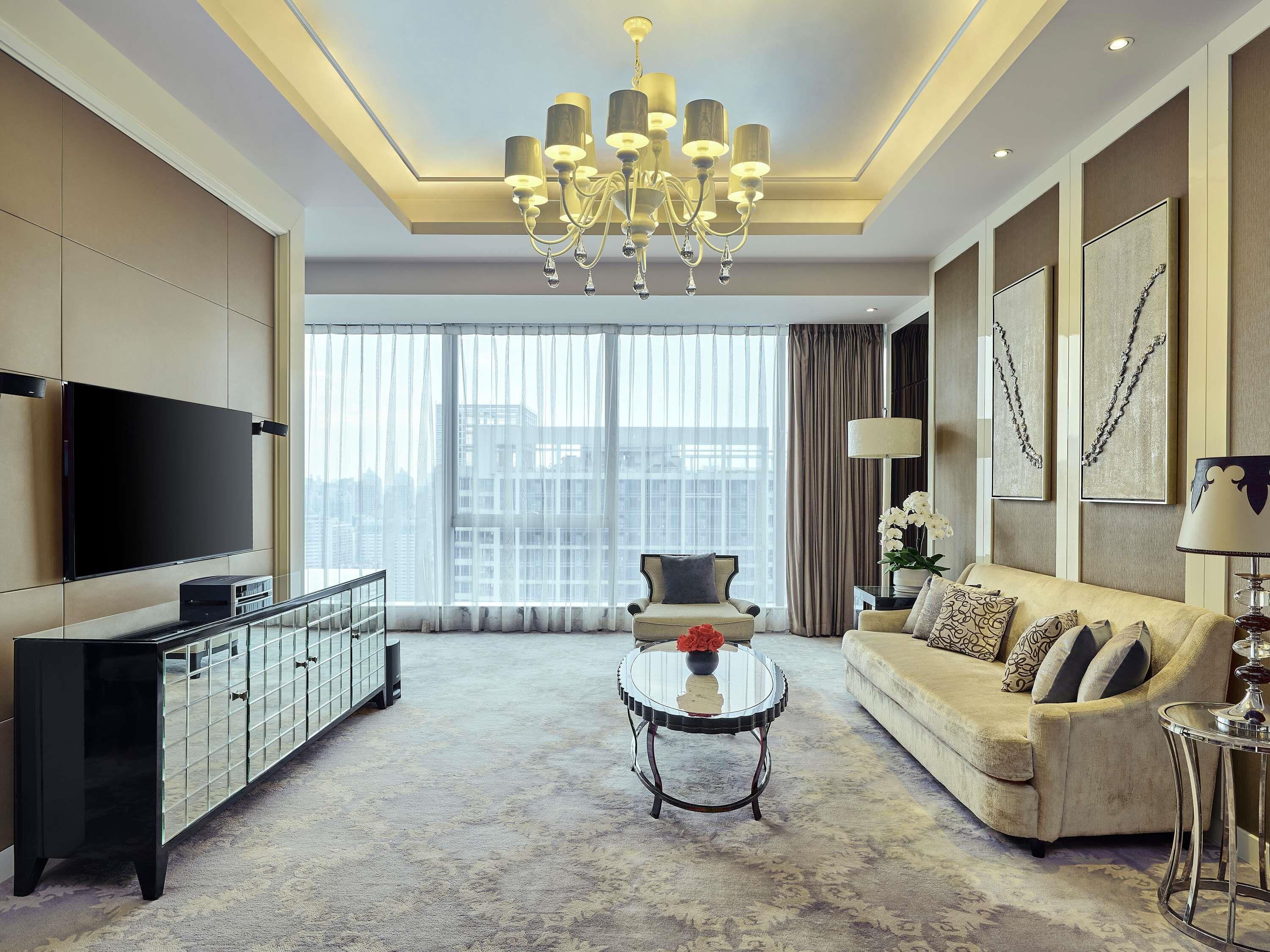 A modern living room with a large flat-screen TV, a sofa, a coffee table, and a chandelier.