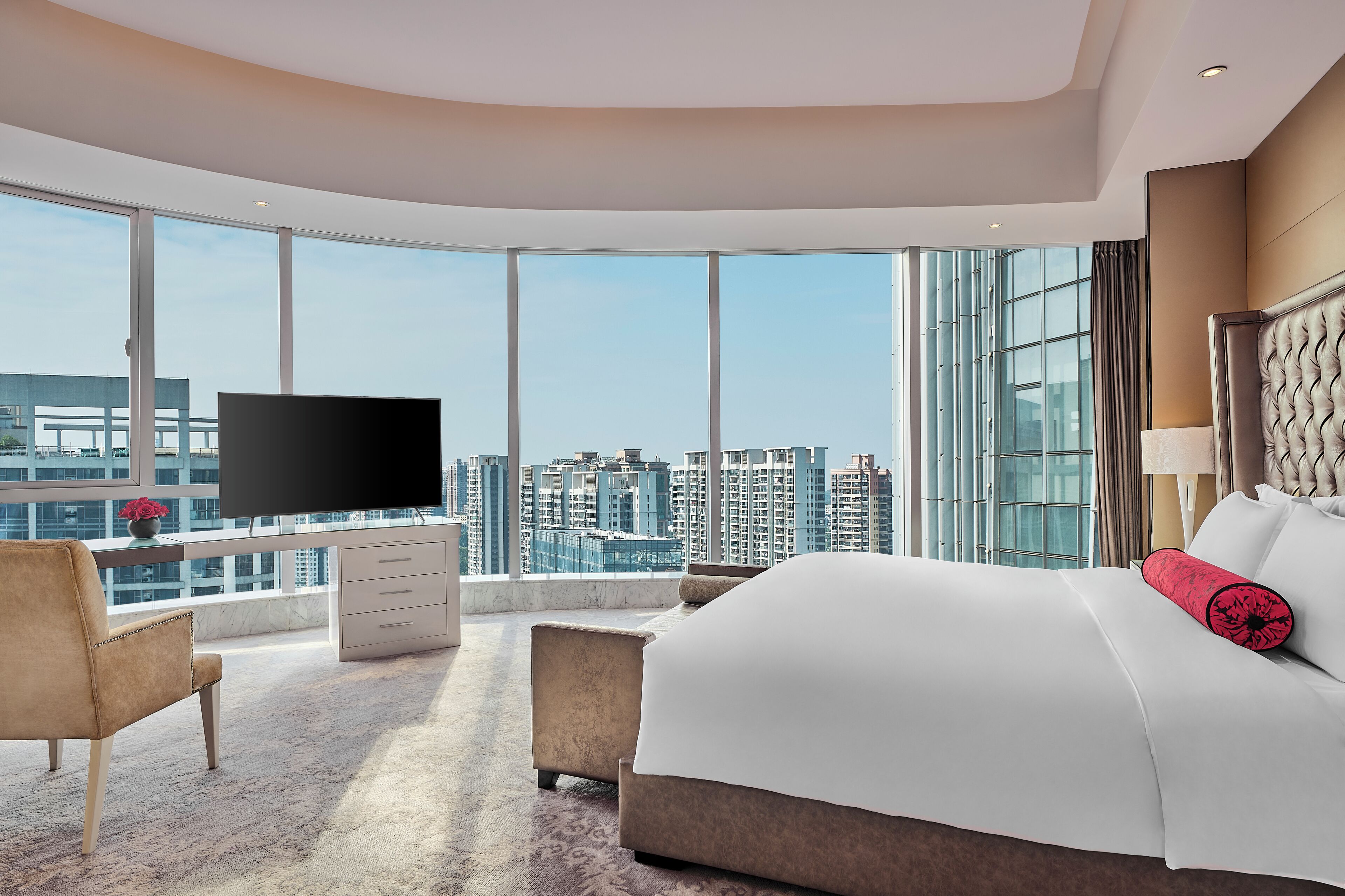 Une chambre d’hôtel moderne dotée d’un grand lit, d’un bureau avec un téléviseur à écran plat et offrant une vue sur le paysage urbain grâce à de grandes fenêtres.