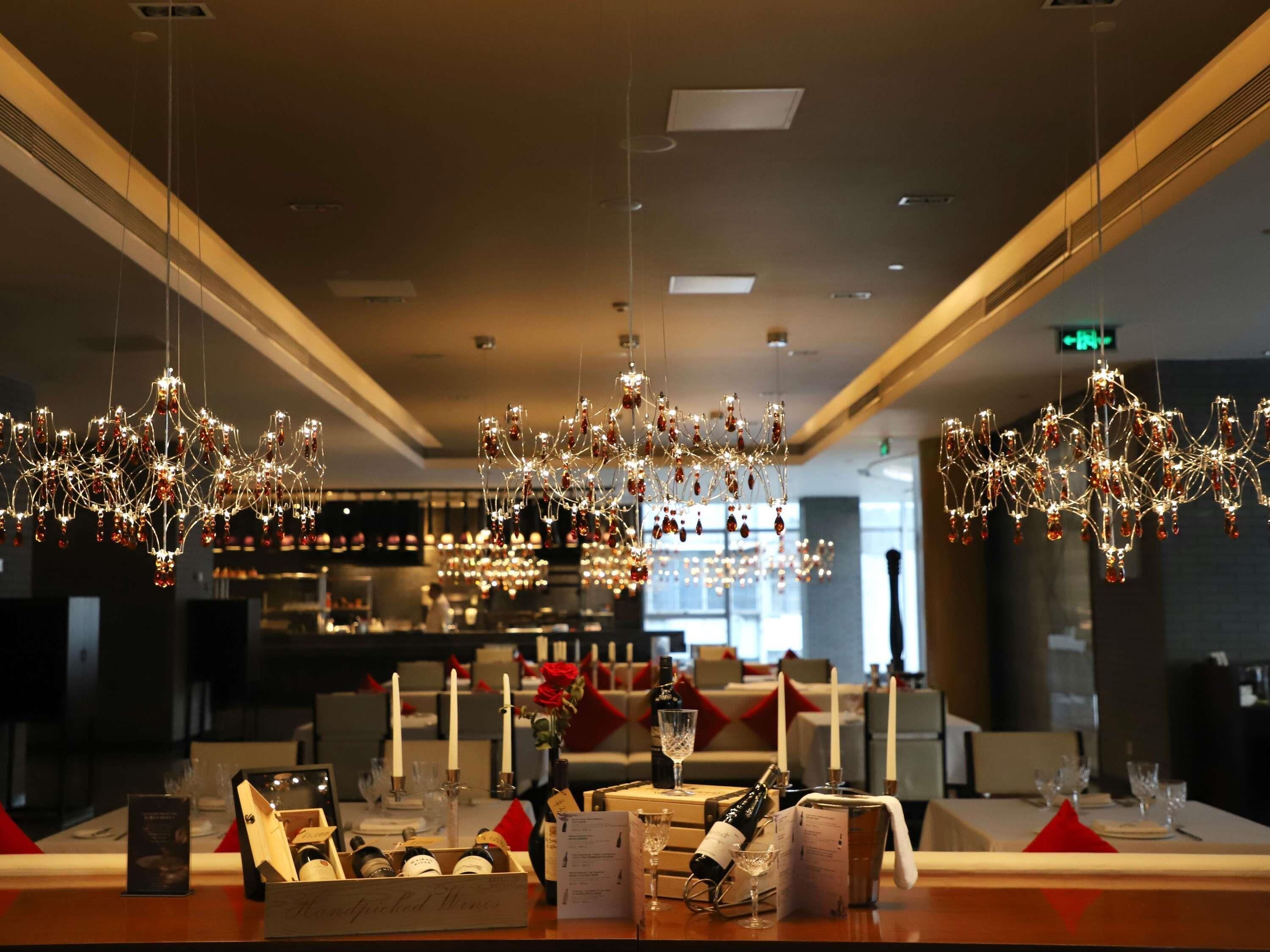 A bar area with hanging chandeliers, bottles of wine, glasses, and a menu on the counter.
