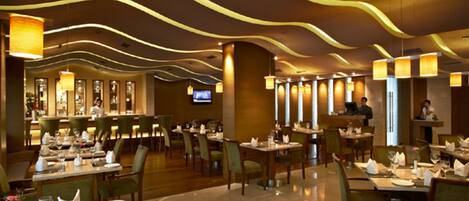 Un restaurante moderno con un diseño de techo curvo y elegante, e iluminación ambiental. Las mesas están dispuestas con impecables servilletas blancas y cristalería.
