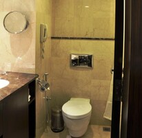 Un baño con lavamanos de mármol, inodoro, ducha de mano y espejo.