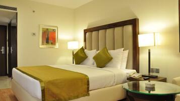 Habitación de hotel con cama, dos lámparas de noche, una mesita de vidrio y un cuadro en la pared.