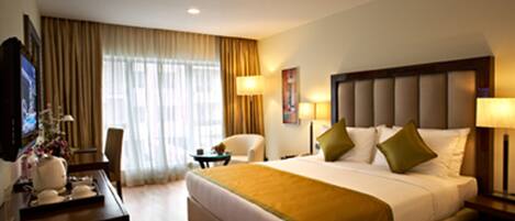 A hotel room with a large bed, a desk with a computer, a chair, and a television.