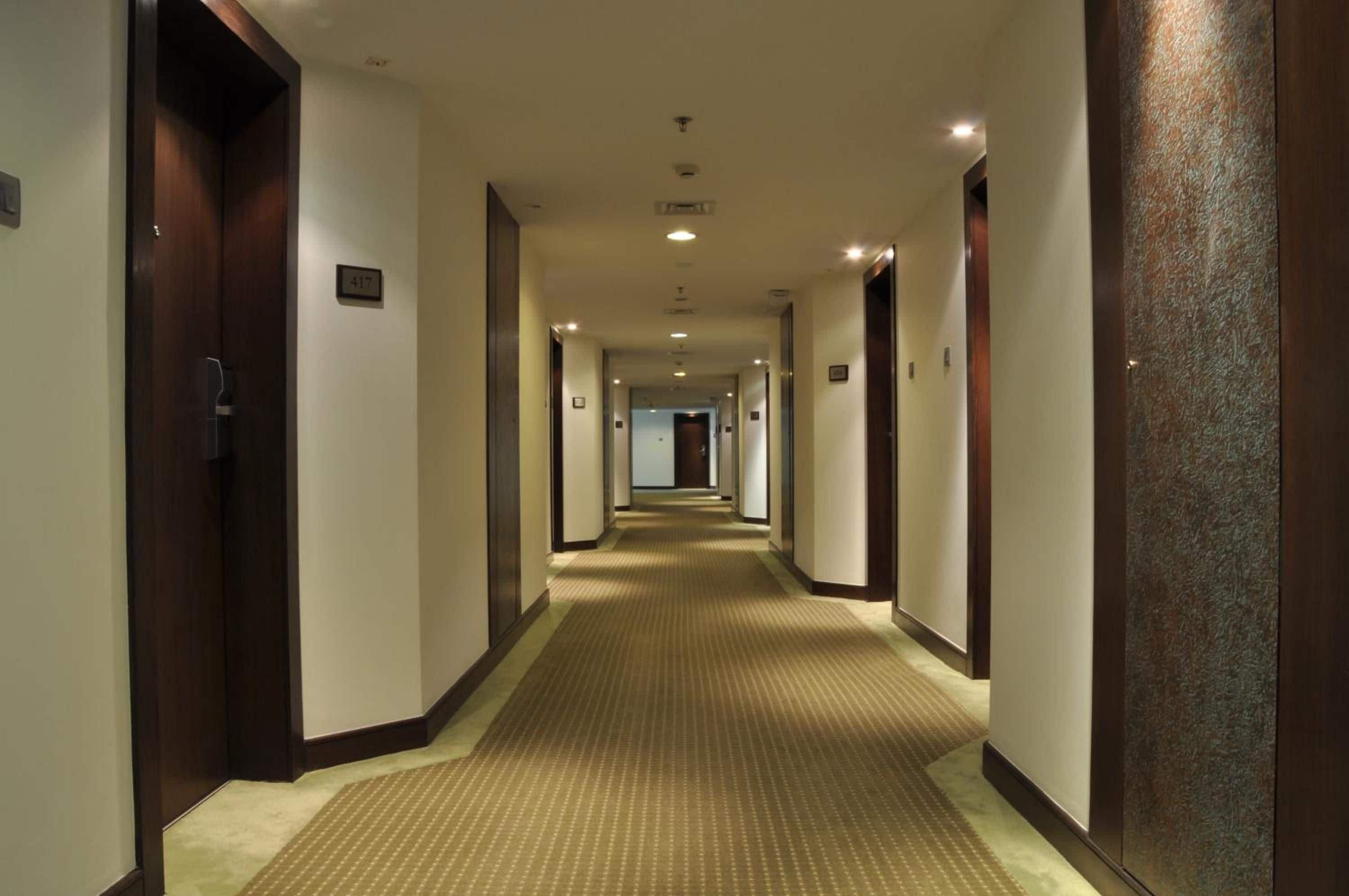 Un pasillo de hotel con pisos alfombrados, puertas a ambos lados y un cartel con números en la pared.