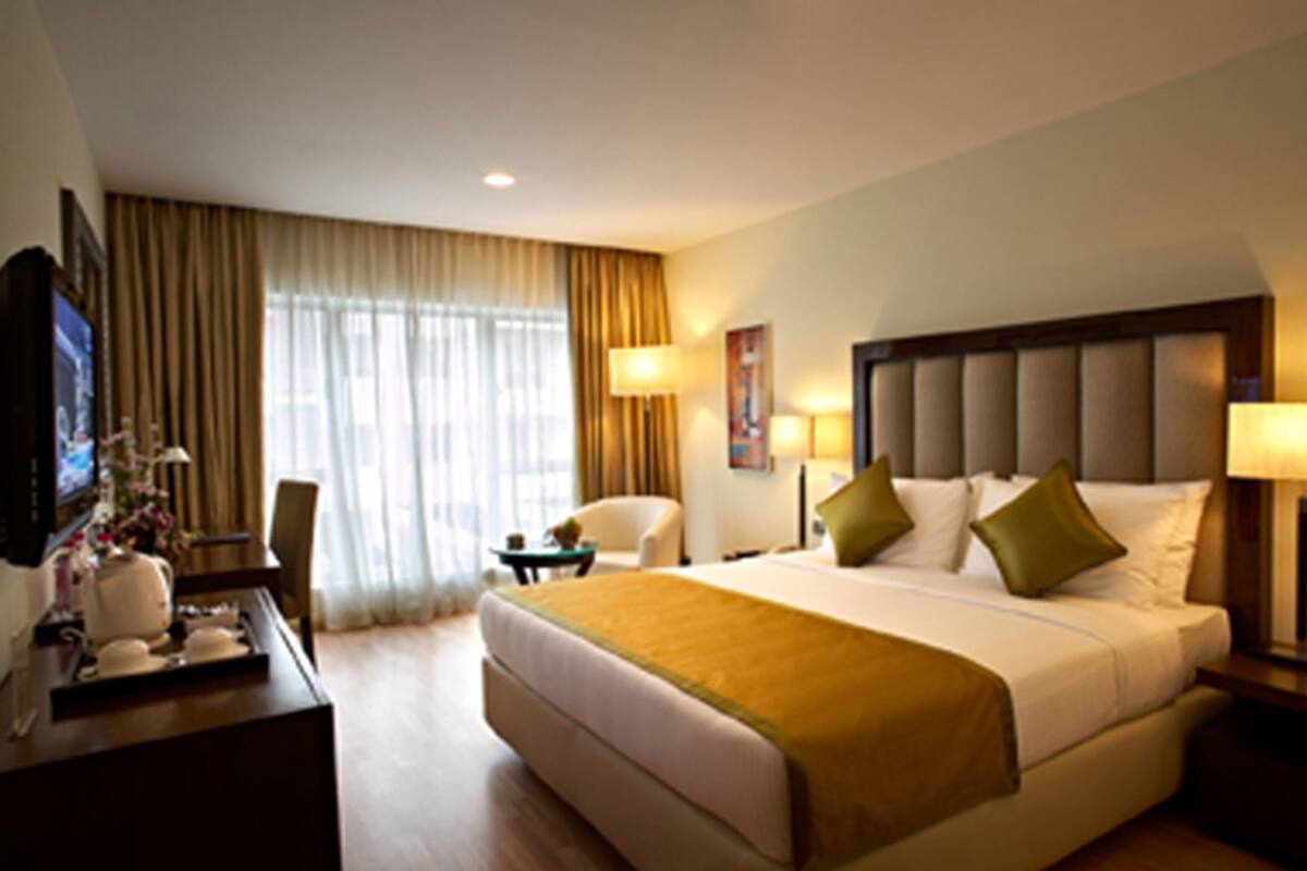 Habitación de hotel con una cama grande, un escritorio con televisor, una silla y una ventana con cortinas.