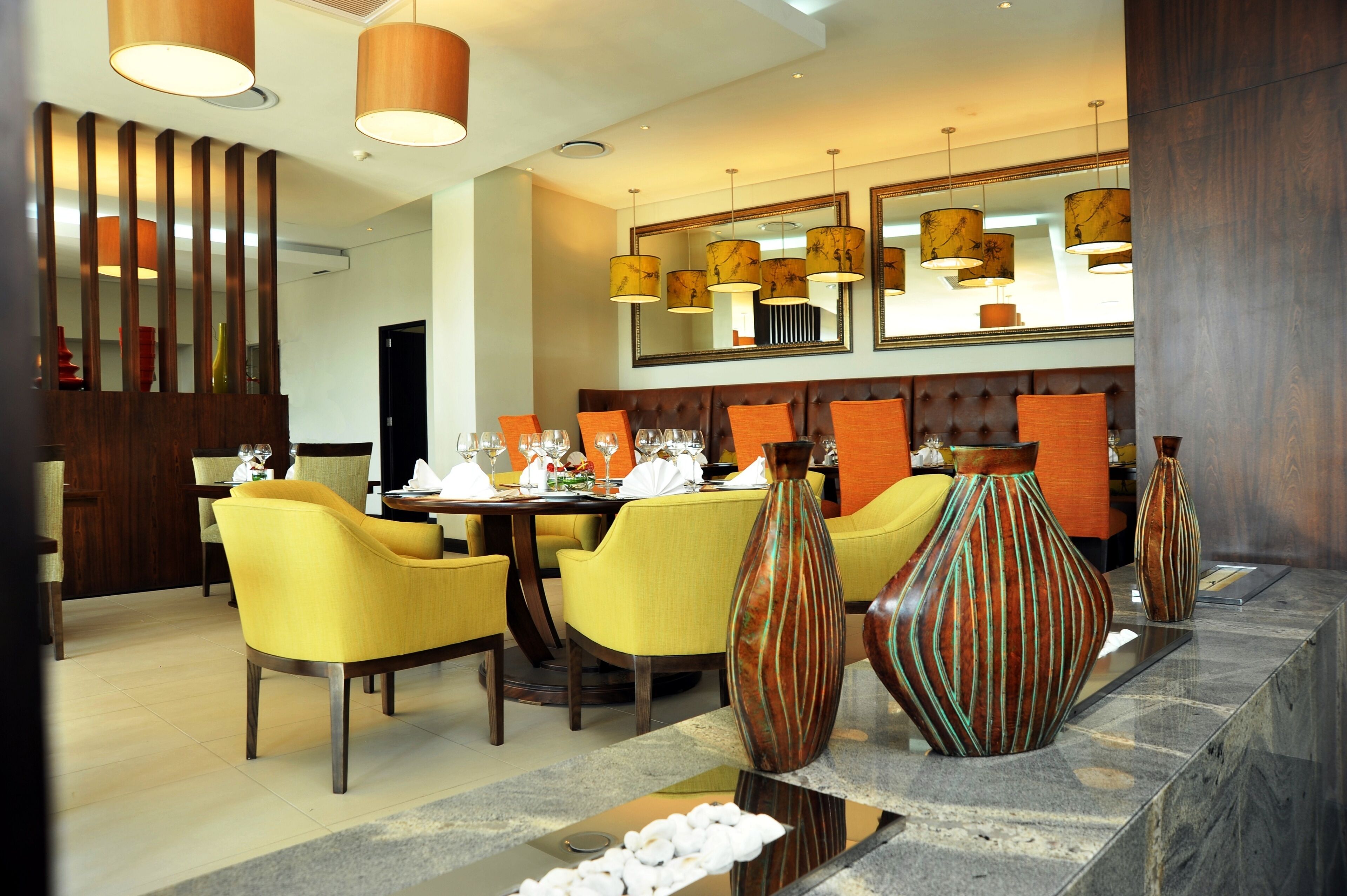 A modern dining area with yellow chairs, a wooden partition, and decorative vases on a marble countertop.