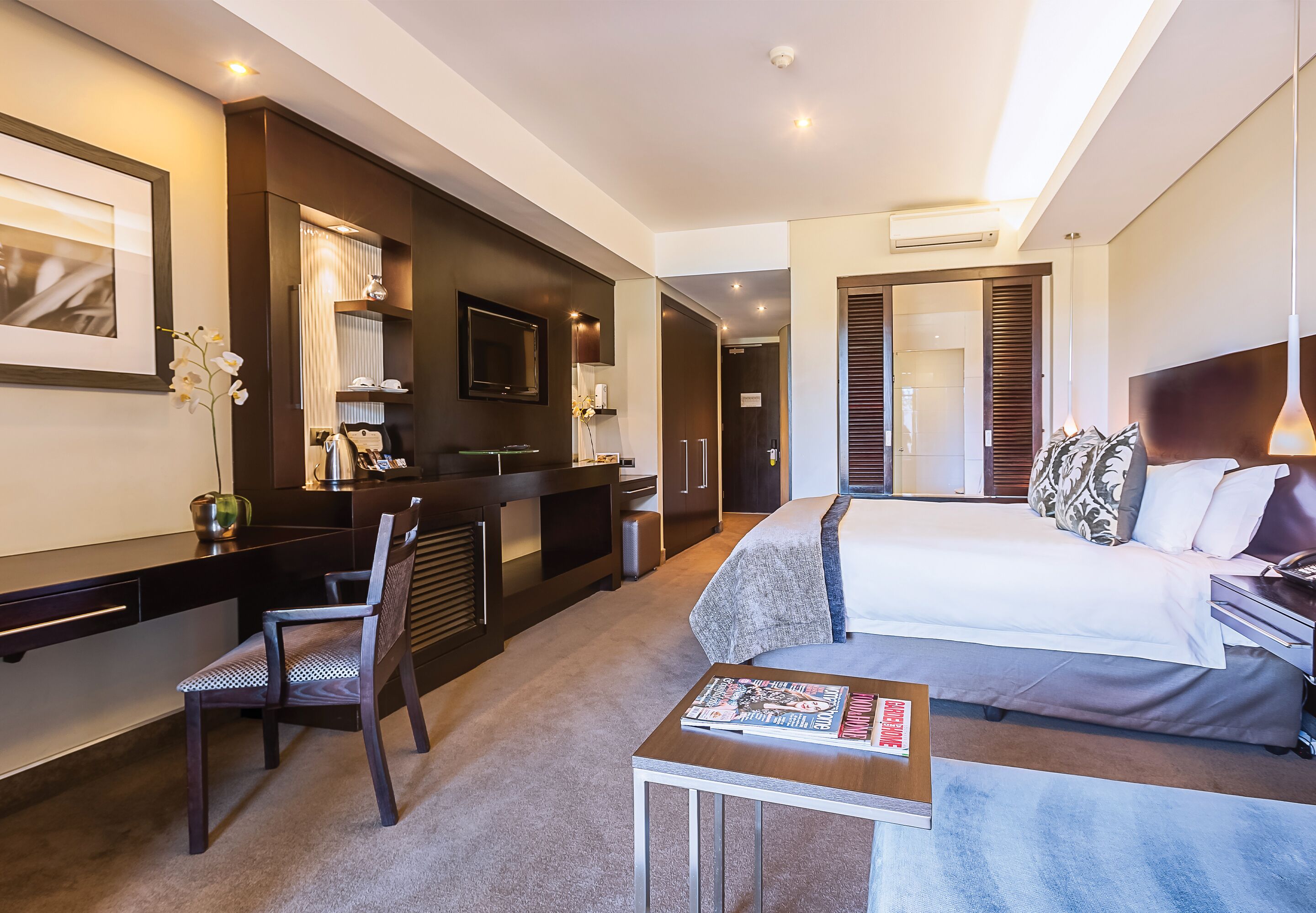 A modern hotel room with a bed, a desk, a chair, and a small table.