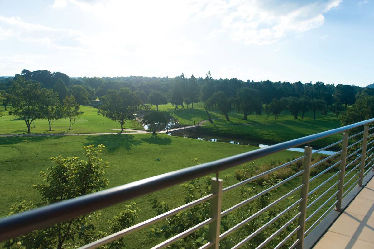 Blick vom Balkon auf eine grüne Landschaft mit Bäumen und einem kleinen Gewässer.