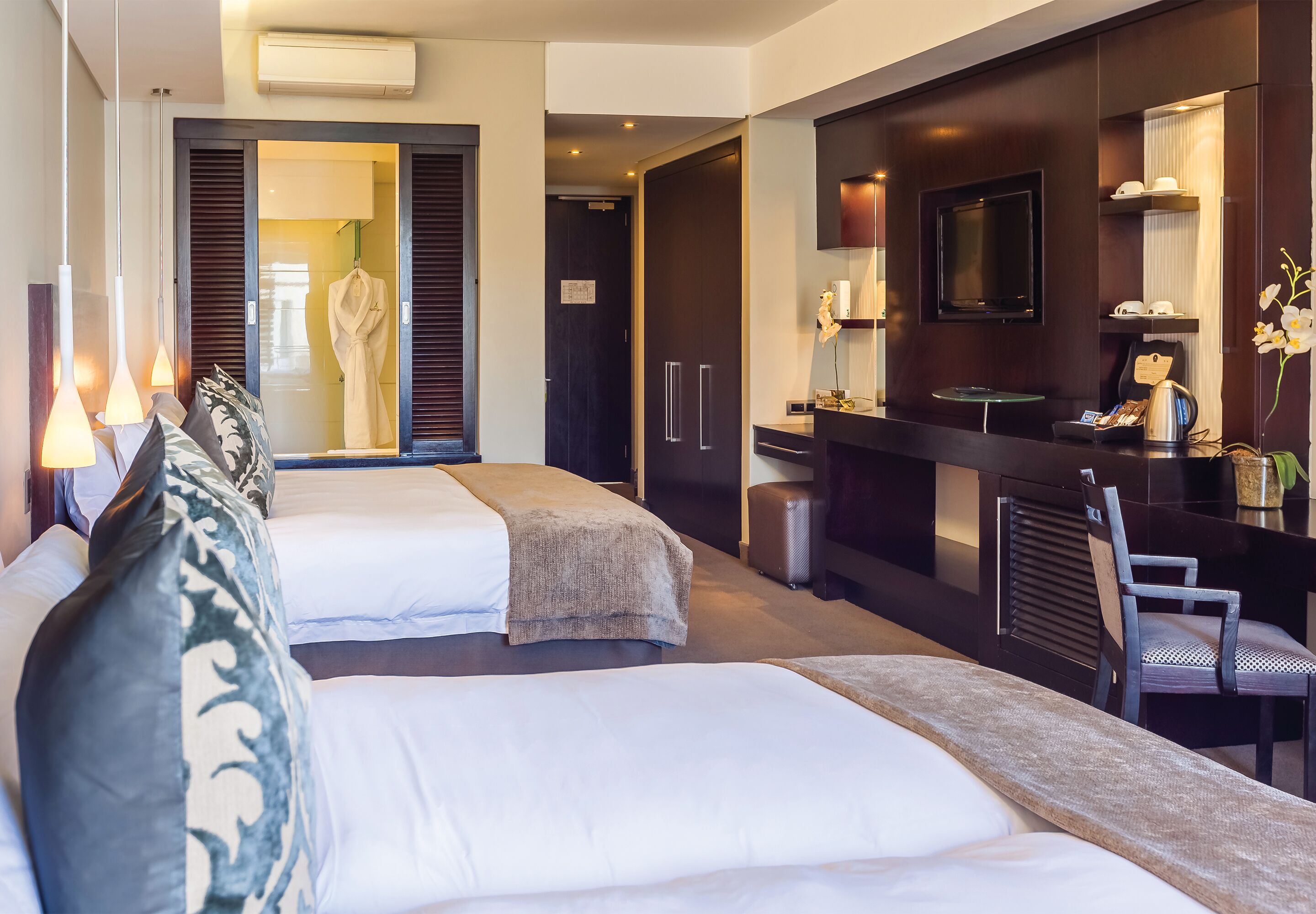 Hotelkamer met twee bedden, een bureau, een stoel, een televisie en een badkamer met een badjas.