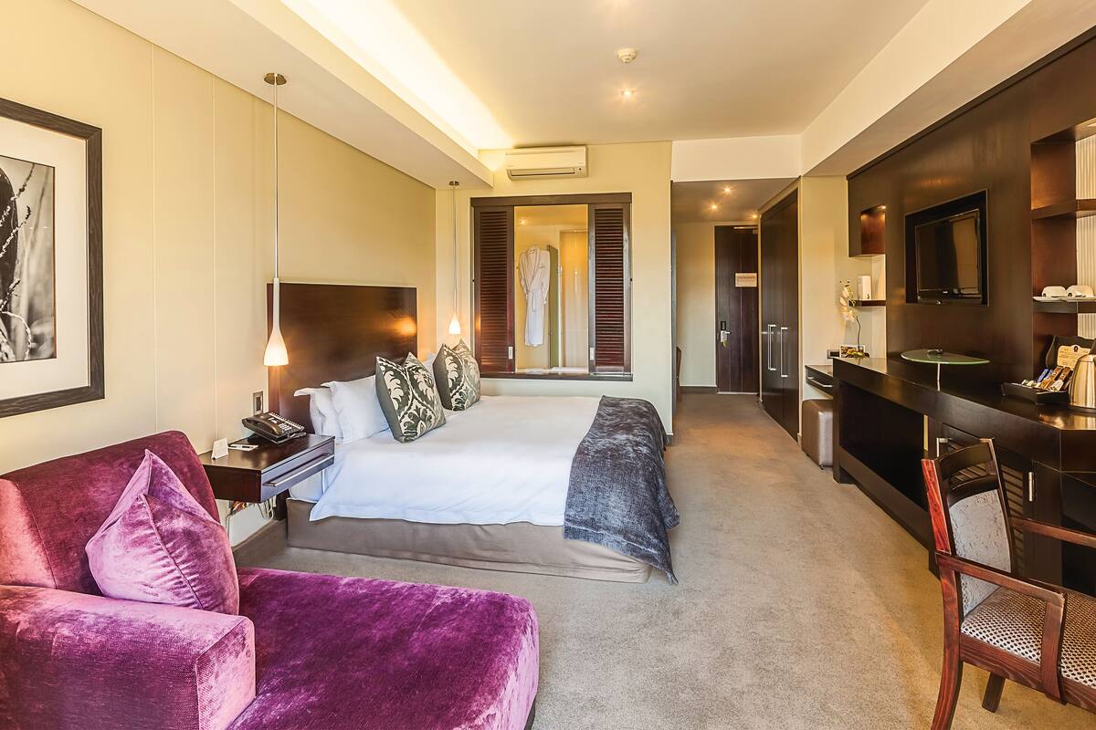 Ein modernes Hotelzimmer mit einem großen Bett, einem Schreibtisch, einem Fernseher und einem durch eine Tür sichtbaren Badezimmer.