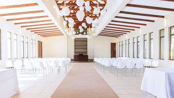 Un amplio salón con sillas blancas dispuestas en filas, un pasillo central y un techo de madera con decoraciones esféricas colgantes.