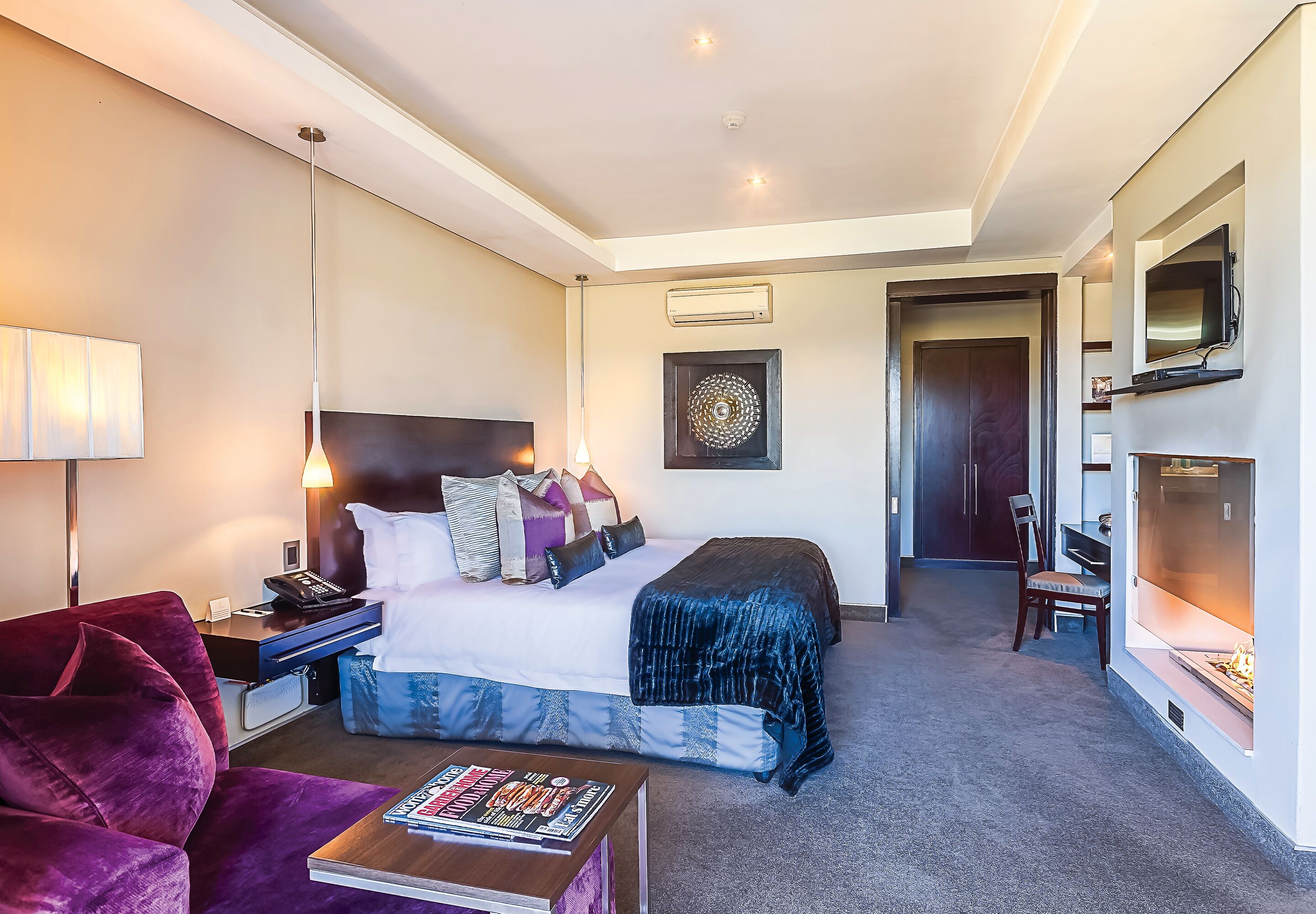 Une chambre d’hôtel avec un lit, un bureau doté d’une lampe, un téléviseur fixé au mur et une cheminée.