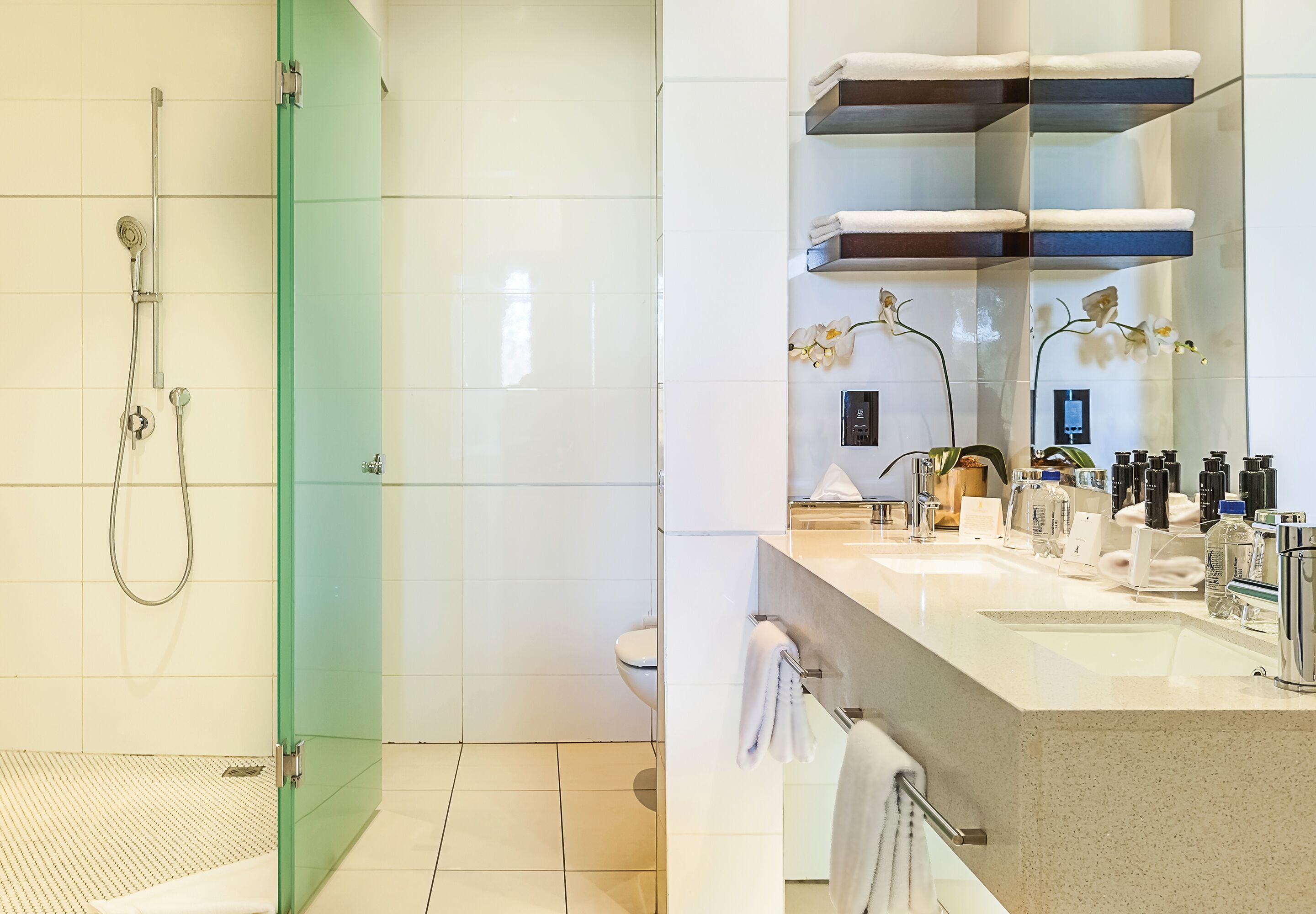Een moderne badkamer met een glazen douchecabine, toilet, wastafel met spiegel en een handdoekrek.