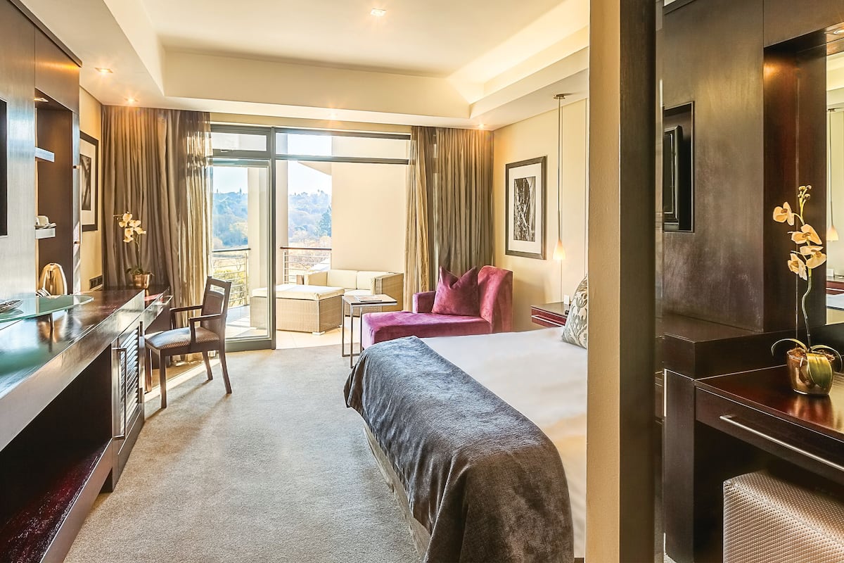Ein Hotelzimmer mit Bett, Schreibtisch, Sessel und einer Aussicht ins Freie.