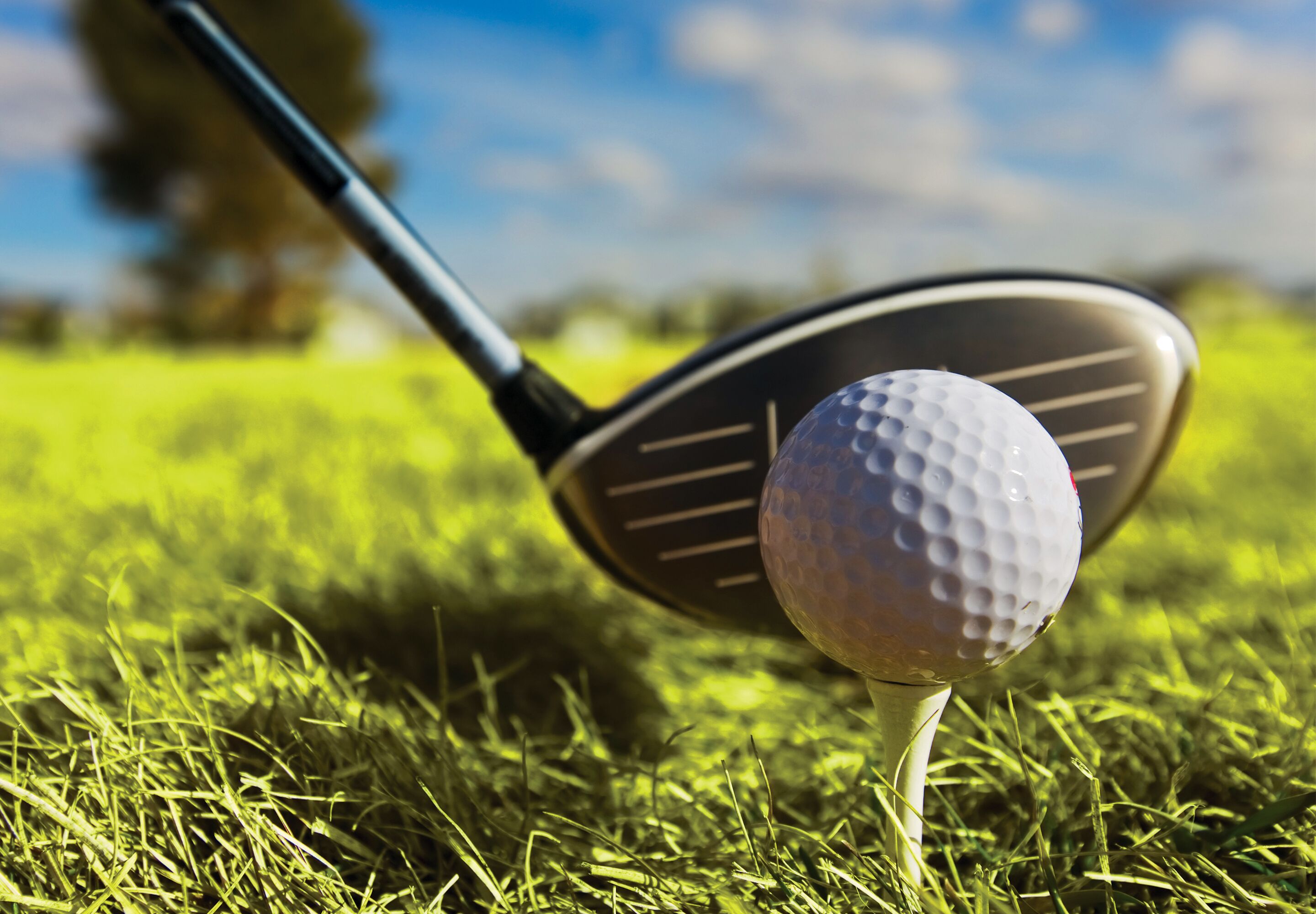 A golf ball on a tee in a grassy area with a golf club nearby.