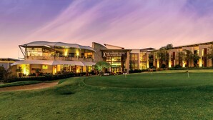 Ein modernes Hotel mit gut beleuchteter Fassade, einem Golfplatz im Vordergrund und klarem Himmel im Abendrot.