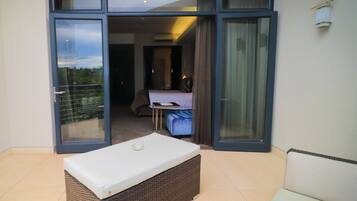 A room with a bed, a small table, and a bench. There is a sliding glass door leading to an outdoor area.
