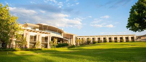 A modern building with a curved roof and multiple windows, surrounded by a well-maintained lawn and trees.