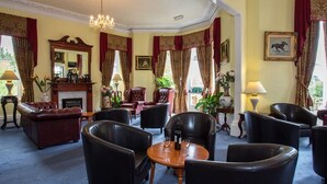 En klassisk hotellobby med läderfåtöljer, en öppen spis och en kristallkrona.