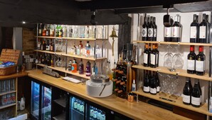 Zona de bar con estantes llenos de botellas de licores, vasos y un refrigerador abastecido de bebidas.