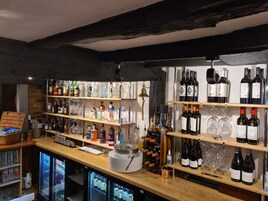 Zona de bar con estantes llenos de botellas de licores, vasos y un refrigerador abastecido de bebidas.