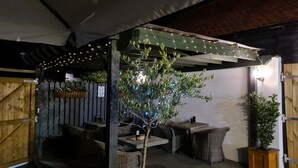 Un espacio exterior con mobiliario de mimbre, luces colgantes y follaje.