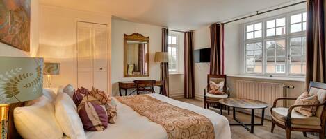 A hotel room with a large bed, a desk, a chair, and a window with curtains.