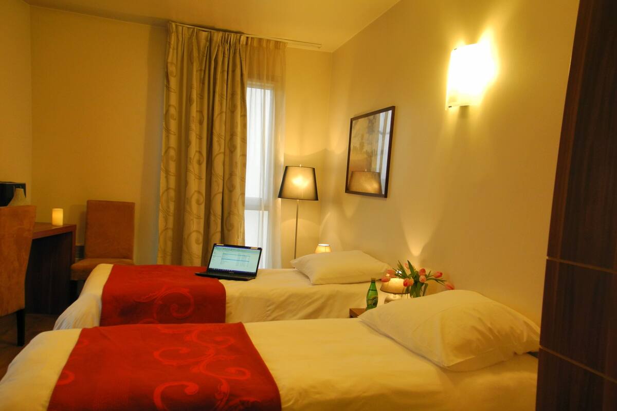 Une chambre d’hôtel avec deux lits, un bureau avec un ordinateur portable, une chaise, une lampe et un tableau accroché au mur.