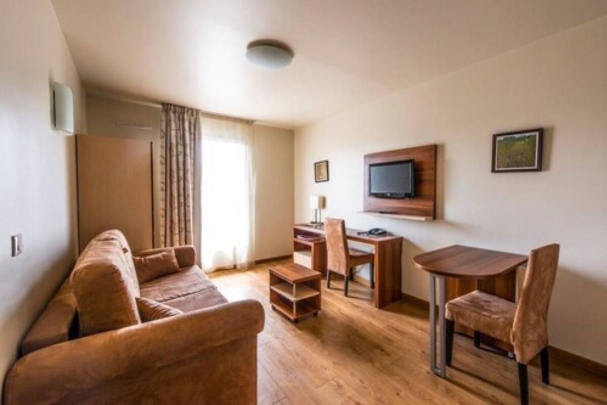 Un espace de vie compact comprenant un canapé, une petite table à manger, un téléviseur fixé au mur et un bureau avec une chaise.