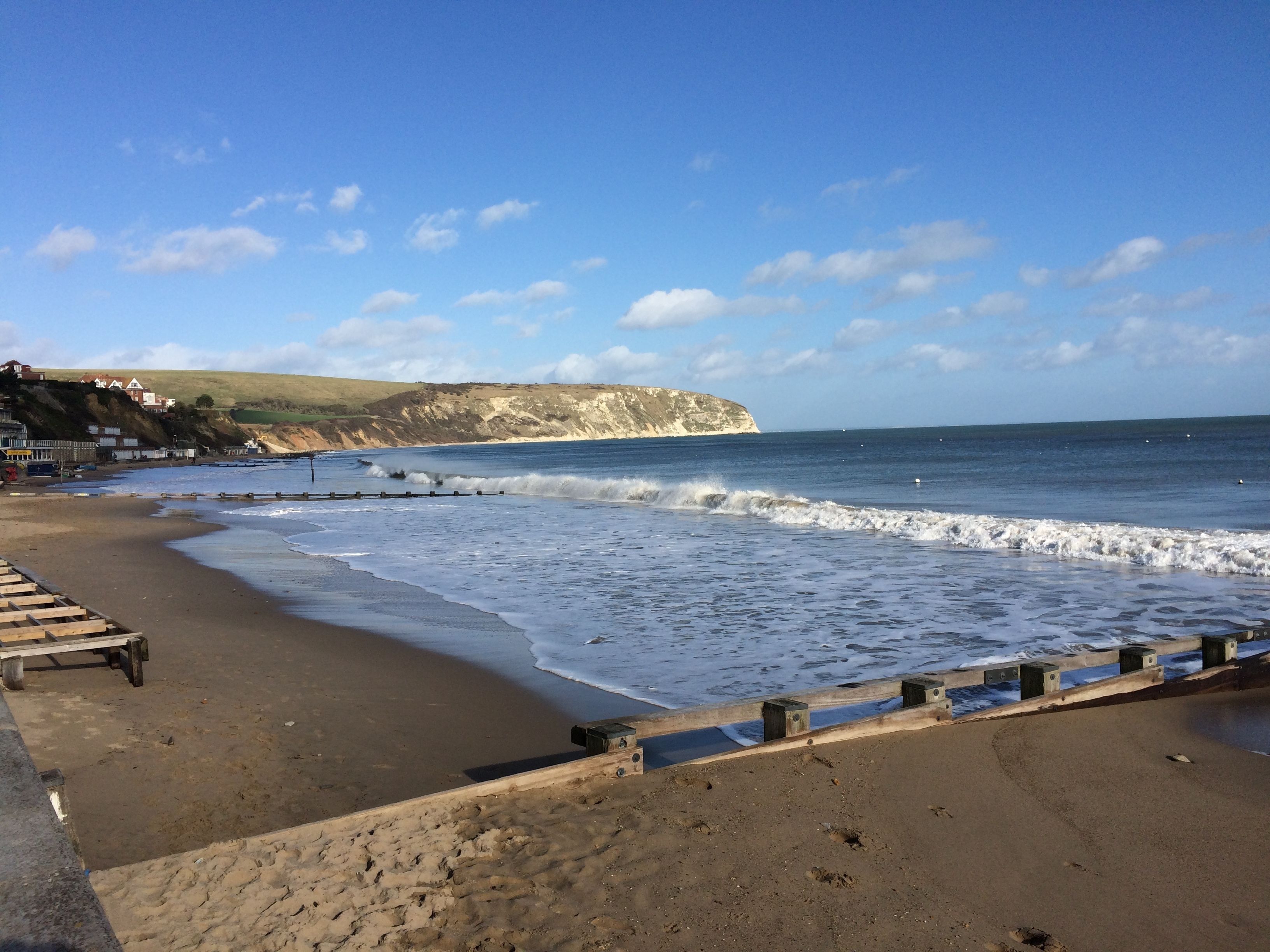 A beach with a wooden walkway, a sandy shore, and a cliff in the background.