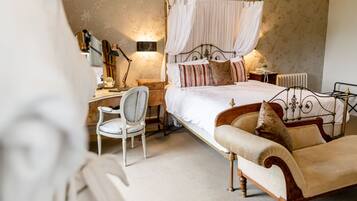 A bedroom with a four-poster bed, a bedside table with a lamp, a chair, and a radiator.