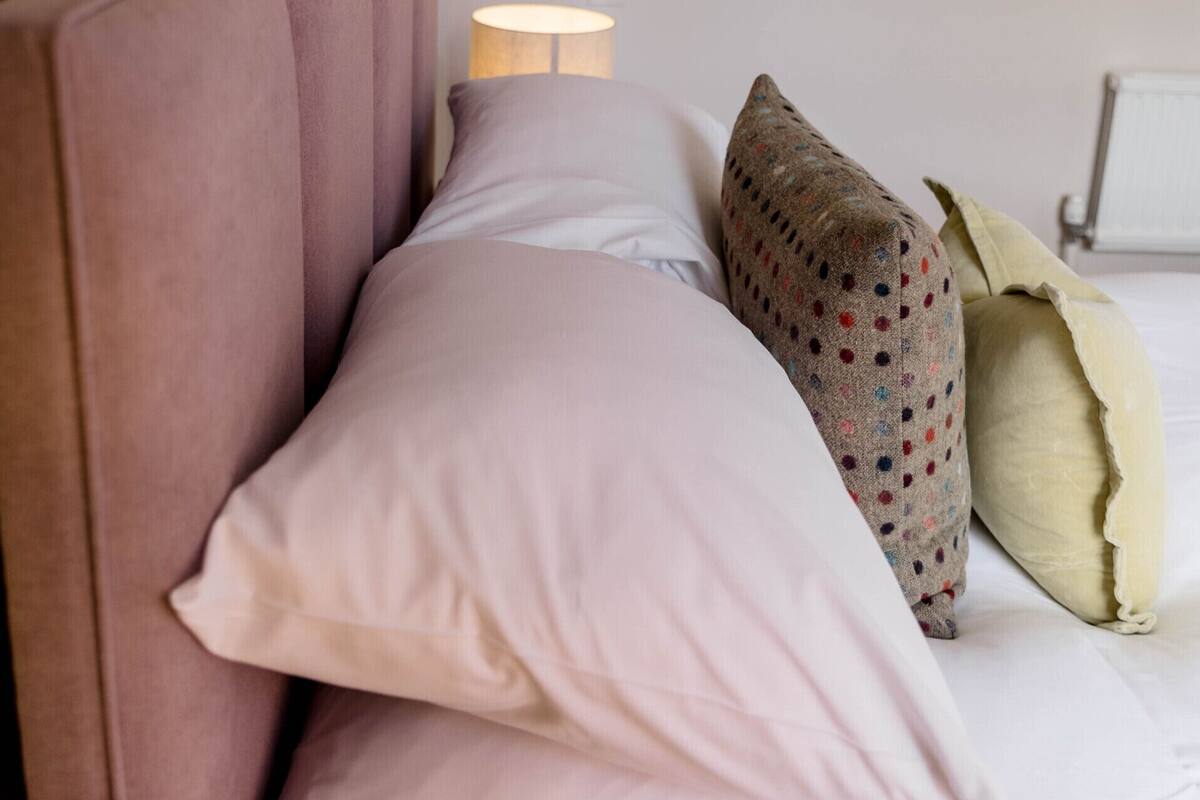 A bedroom with a headboard, two pillows, a polka-dotted pillow, and a lamp.