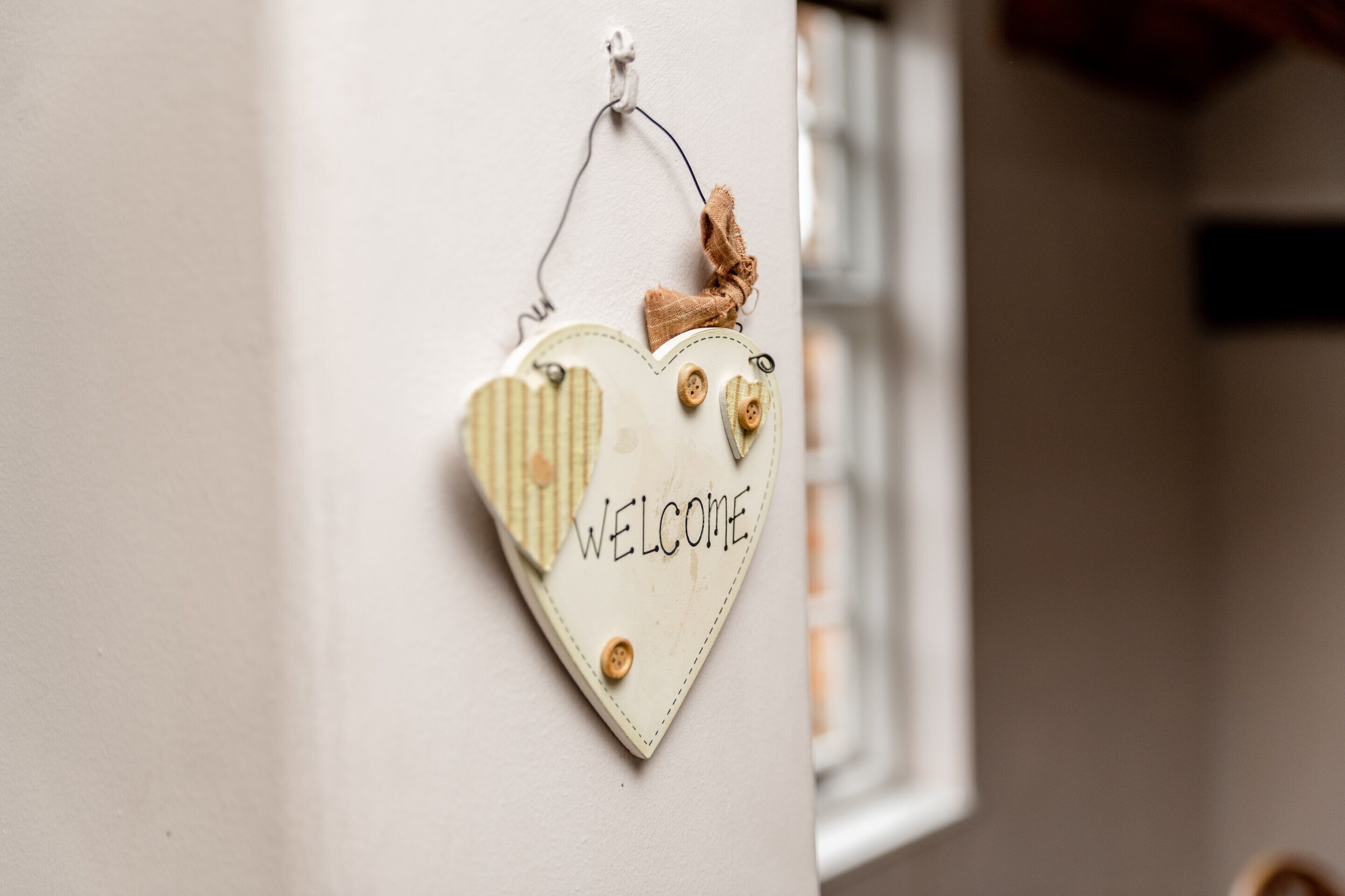 Un letrero de bienvenida con forma de corazón, botones y una cinta sujeta a la pared.