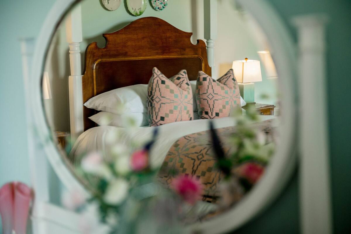 A bedroom with a wooden headboard, patterned pillows, a white bedspread, and a bedside lamp.