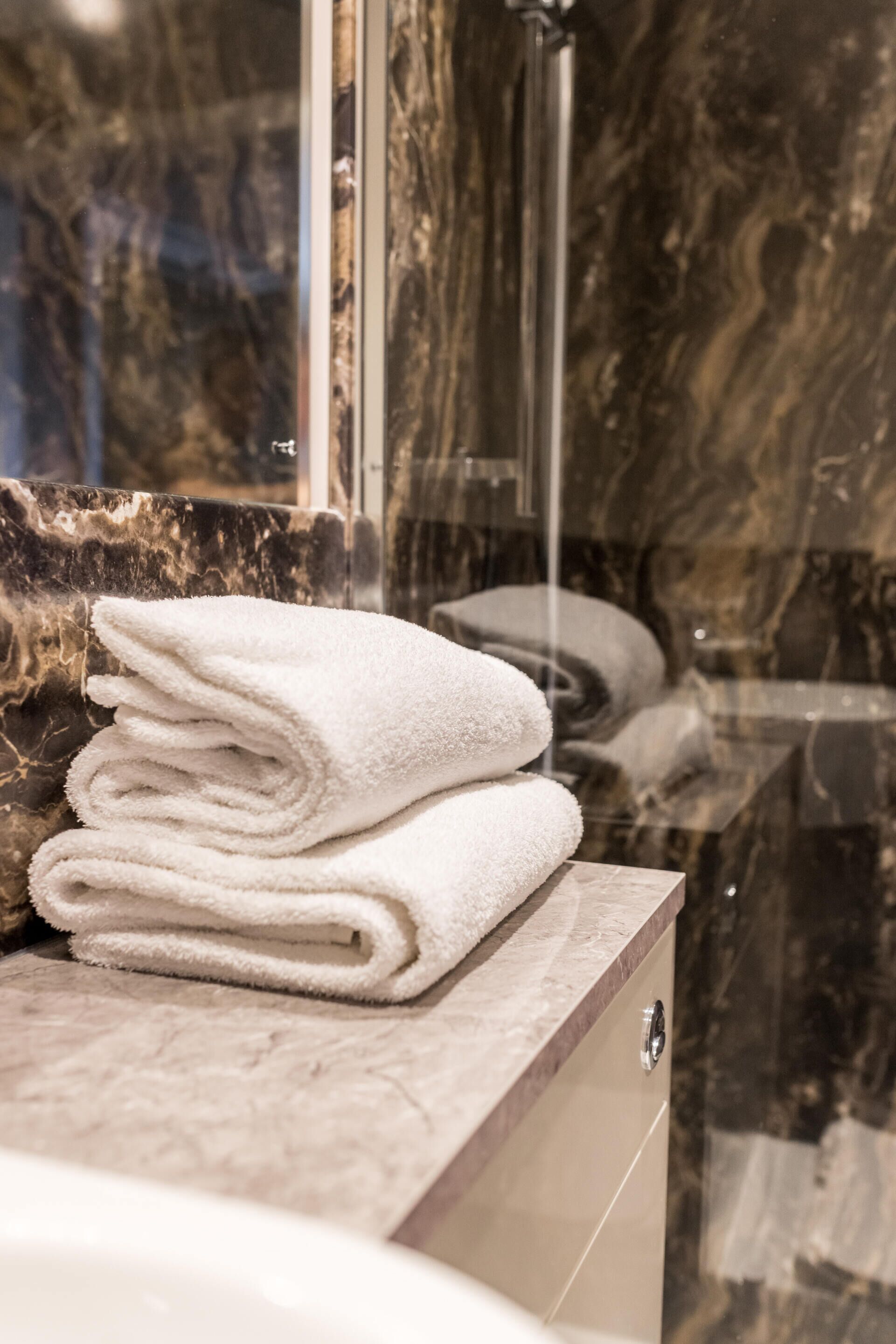 A bathroom with a marble countertop, a stack of white towels, and a glass shower enclosure.