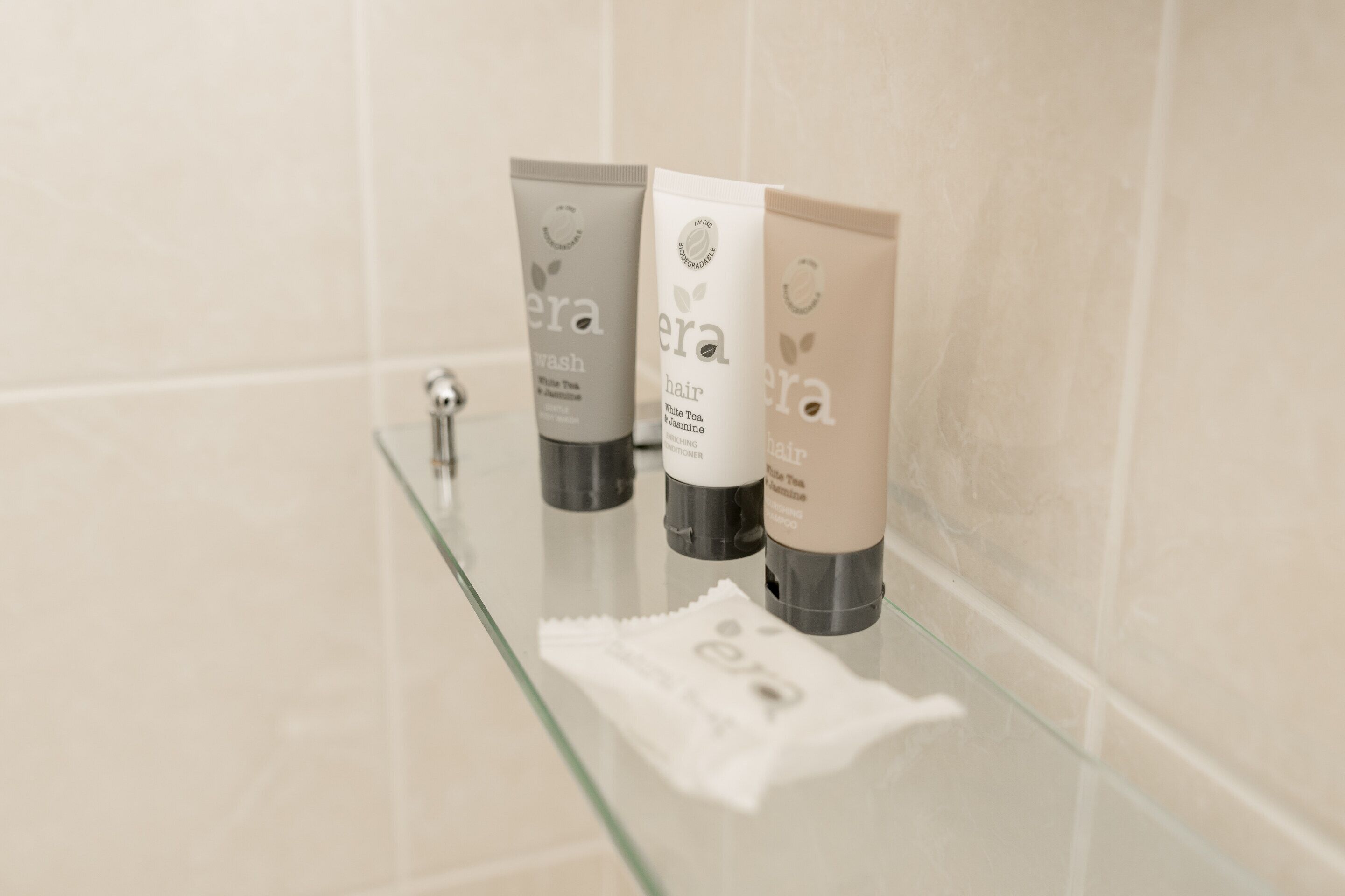 Tres botellas de productos capilares 'era' sobre una repisa de vidrio en un baño.