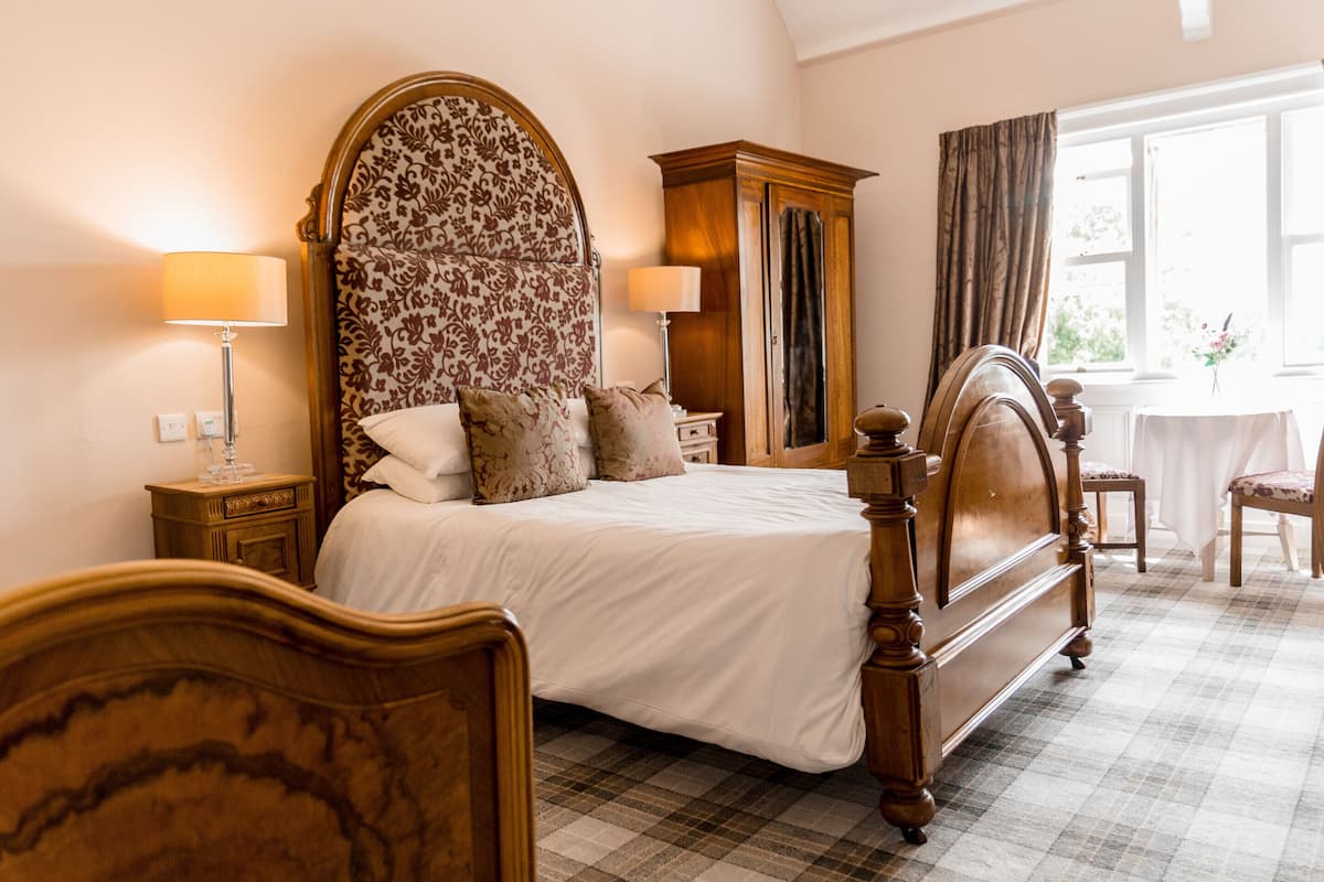 A bedroom with a large bed, wooden headboard, two bedside tables, a nightstand, a wooden wardrobe, and a window with curtains.