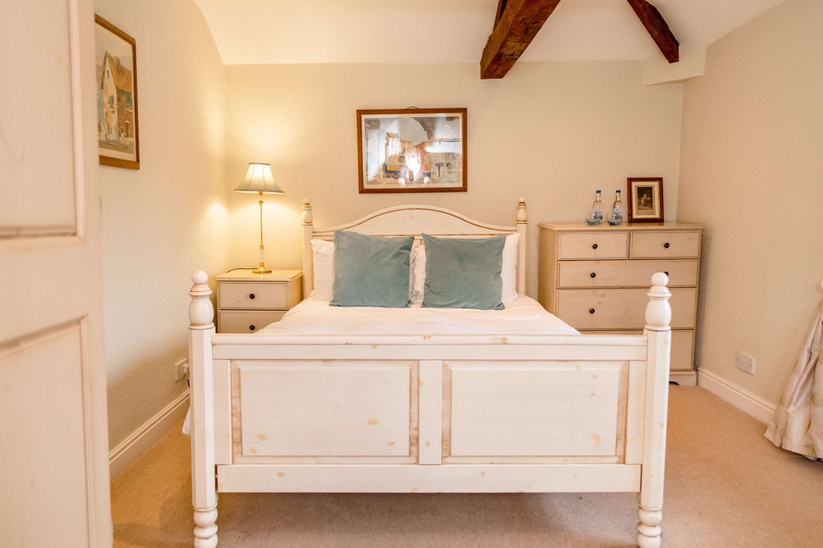 Une chambre à coucher avec un lit à baldaquin blanc, une table de chevet avec une lampe, une commode avec un miroir et un tableau encadré accroché au mur.
