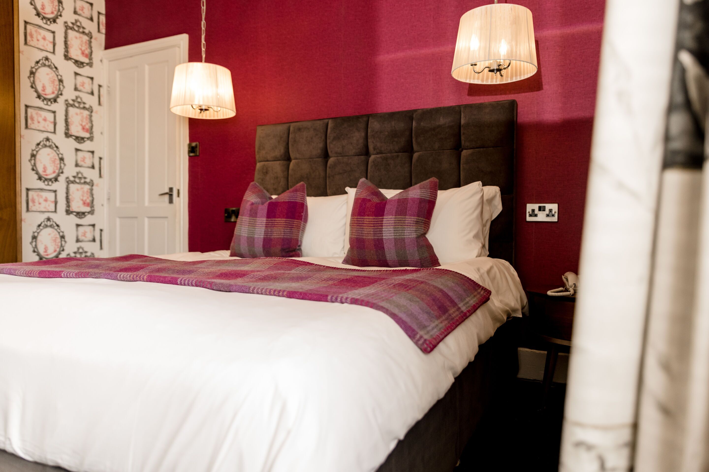 A bed with a white duvet, two purple pillows, and a plaid blanket.