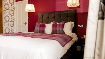 A bed with a white duvet, two purple pillows, and a plaid blanket.