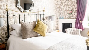 A neatly made bed with a headboard, a mirror above it, and a fireplace in the background. - Sweeney Hall Hotel (Oswestry)