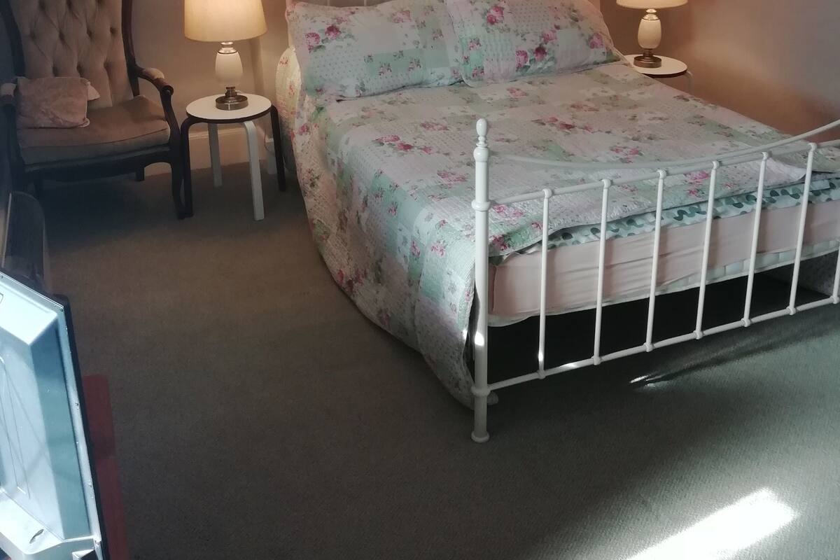 A bedroom with a bed, two bedside tables, a chair, and a picture frame on the wall.